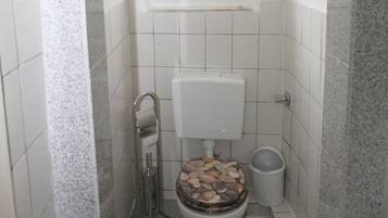 A small bathroom with a toilet, a window, and a trash bin.
