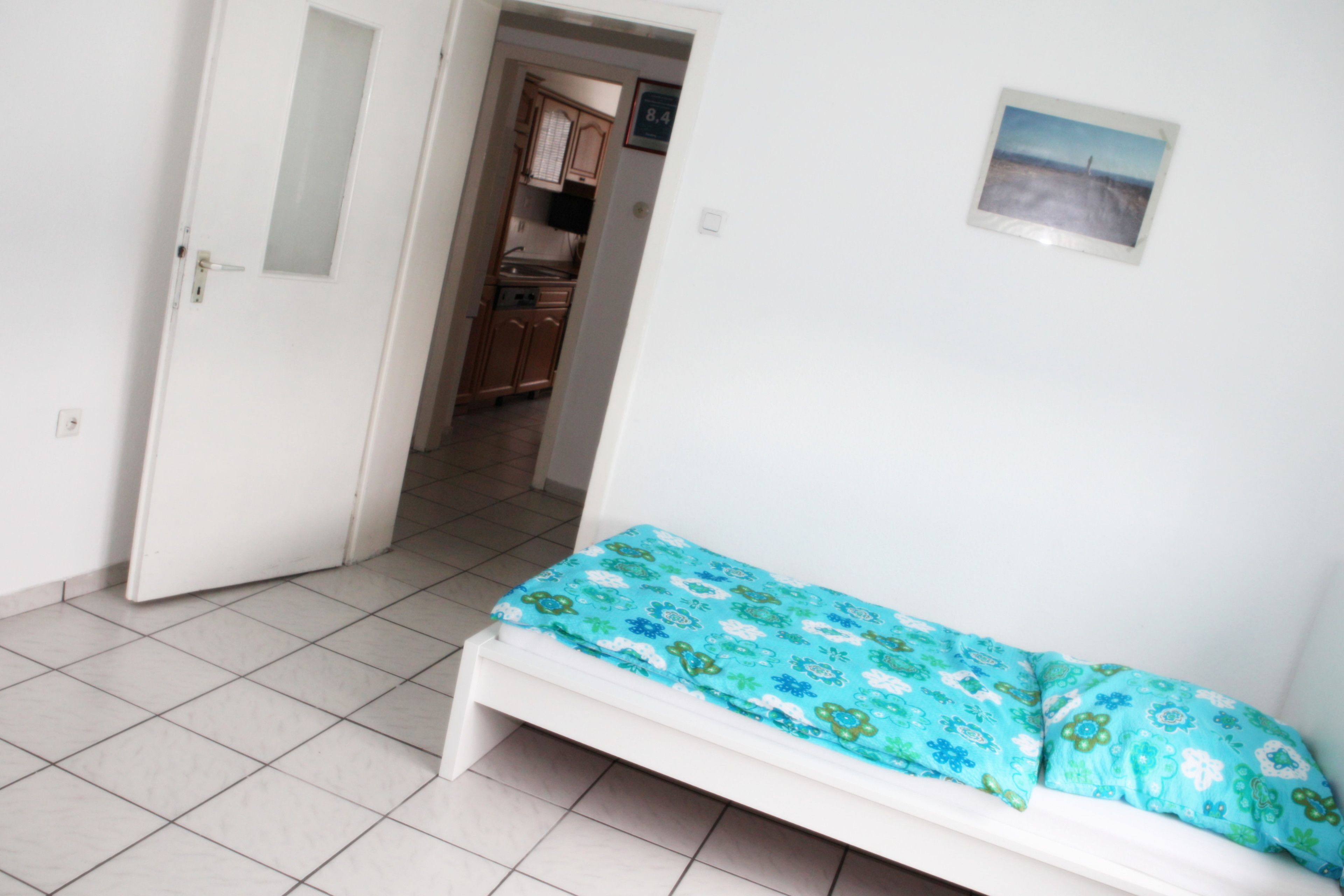 Ein Schlafzimmer mit Bett, einer Tür und Blick in eine Küche.