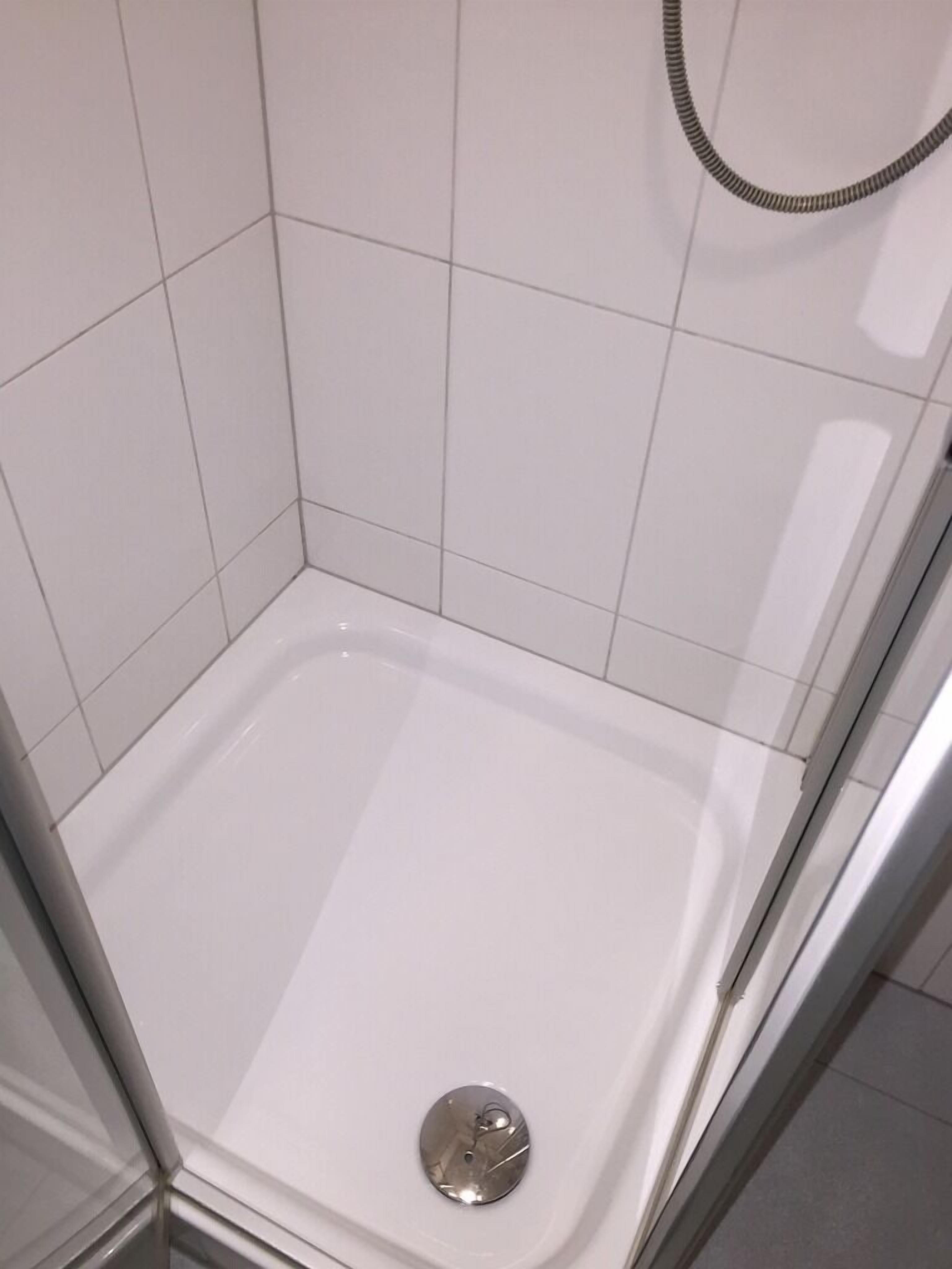 Um chuveiro pequeno revestido de azulejos brancos, com um chuveiro cromado e ralo.