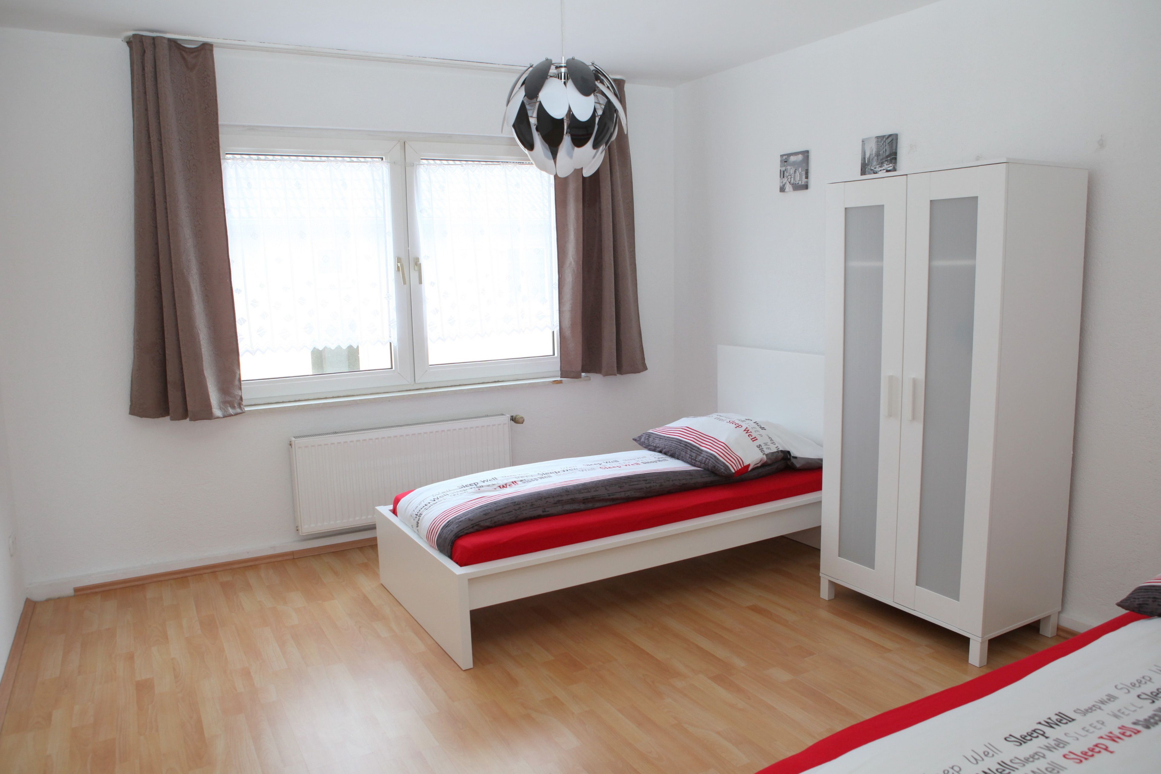 Ein Schlafzimmer mit einem Einzelbett, einem Kleiderschrank, einem Fenster mit Vorhängen und einer Heizung.