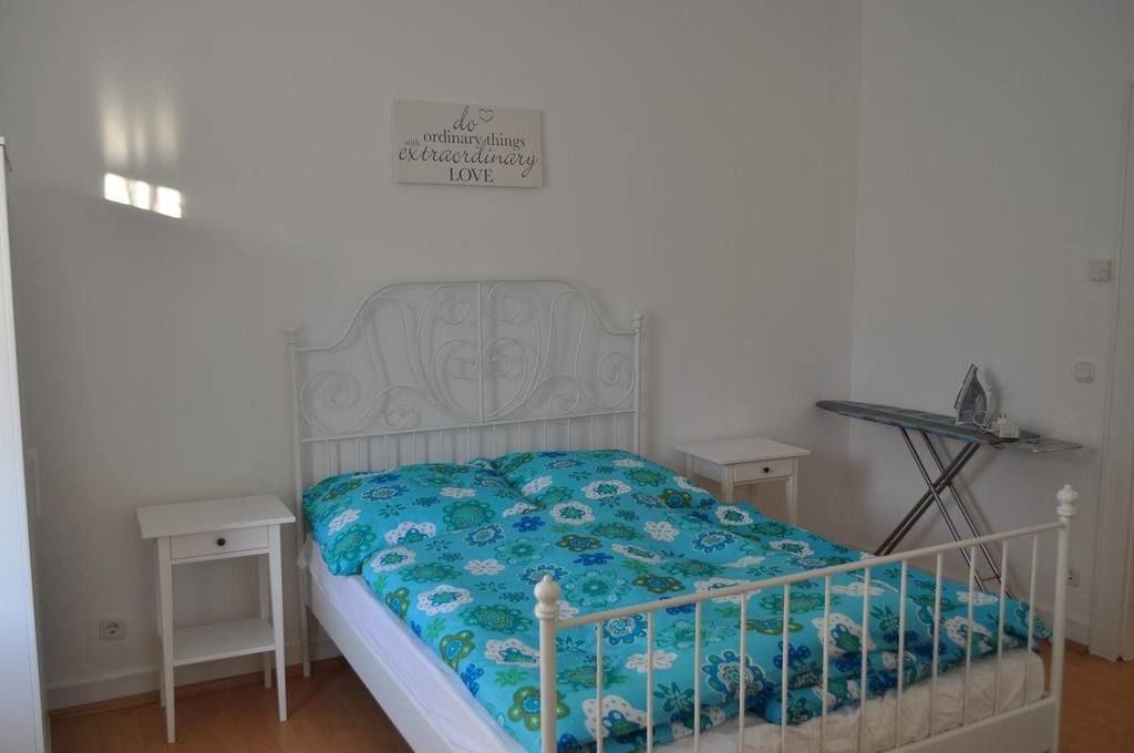 A bedroom with a bed, a nightstand, a wall-mounted ironing board, and a motivational quote on the wall.