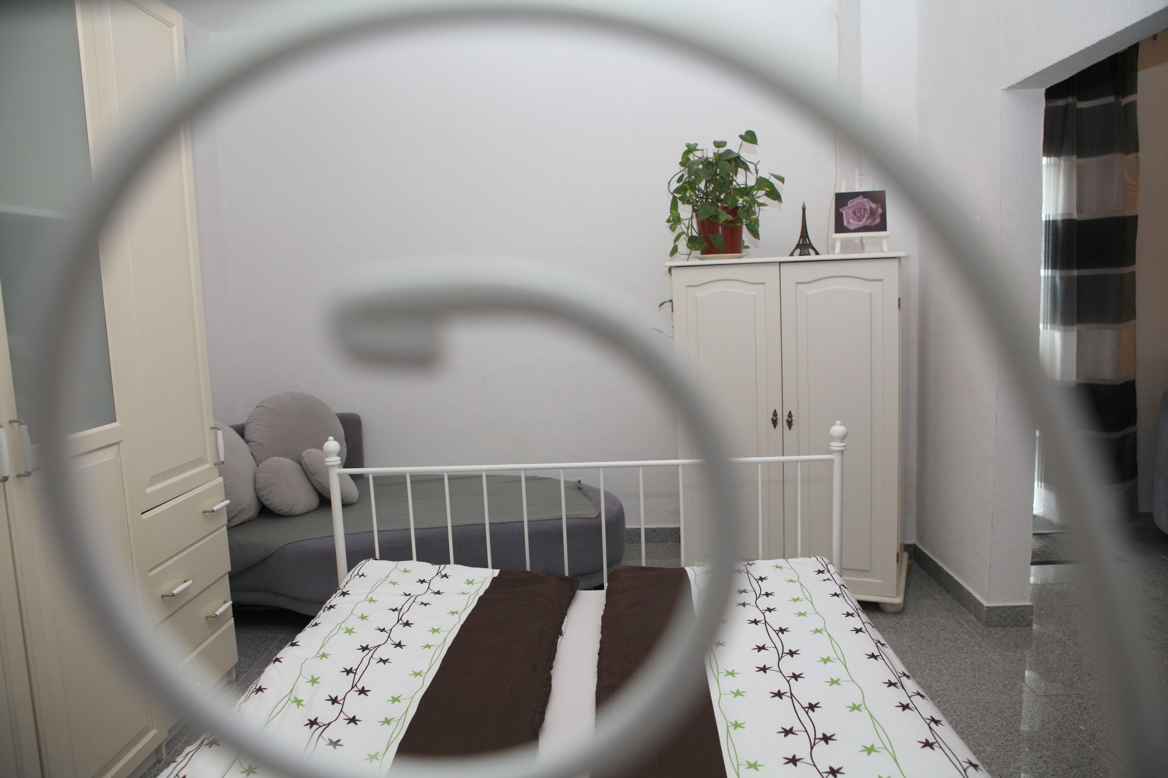 A bedroom with a bed, a wardrobe, a potted plant, and a small Eiffel Tower model on top of the wardrobe.
