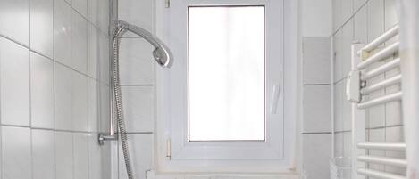 Un baño pequeño con azulejos, ducha, ventana y radiador.