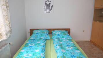 Un lit simple avec une literie à motifs floraux, une tête de lit en bois, un radiateur, une affiche accrochée au mur et une armoire en bois.