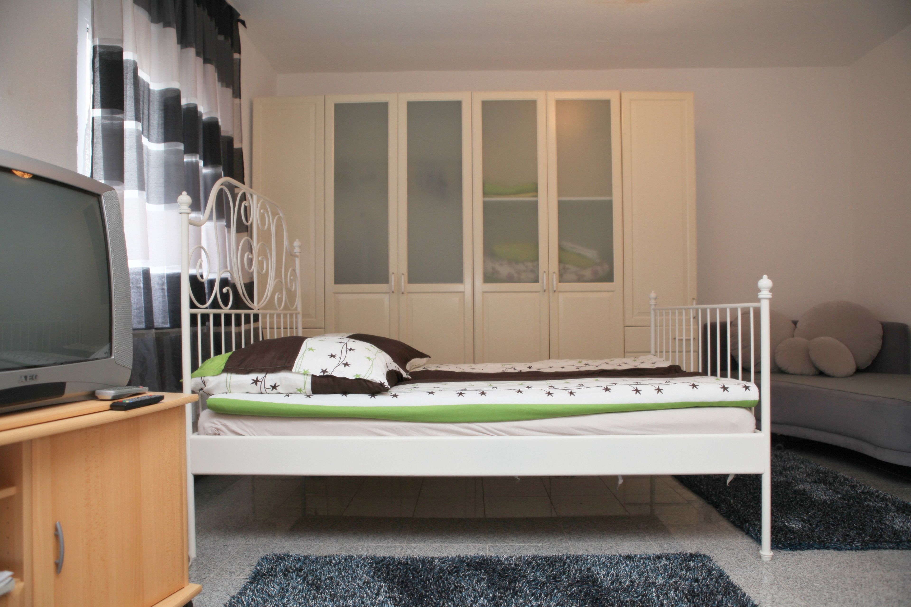 Ein Schlafzimmer mit einem Einzelbett, einem Fernseher auf einem Holzboden und einem Kleiderschrank mit satinierten Glastüren.