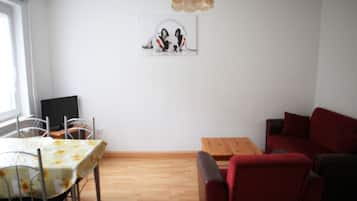 A room with a dining table, chairs, a red sofa, a wooden coffee table, and a wall-mounted picture of a dog wearing headphones.
