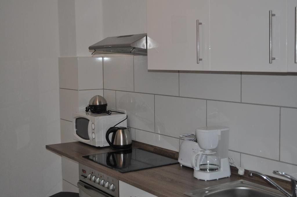A modern kitchen with white cabinets, a microwave, a kettle, a coffee maker, and a stove.