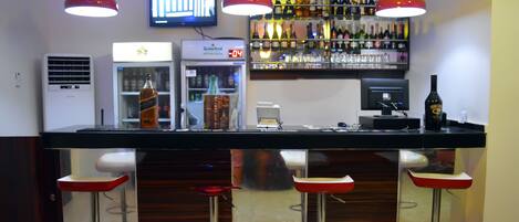 A bar area with a digital screen, a refrigerator, and a variety of bottles.