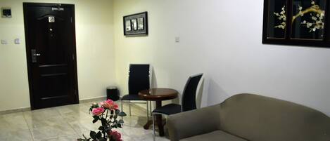 A living room with a sofa, a coffee table with a flower arrangement, a dining table with chairs, and a door.