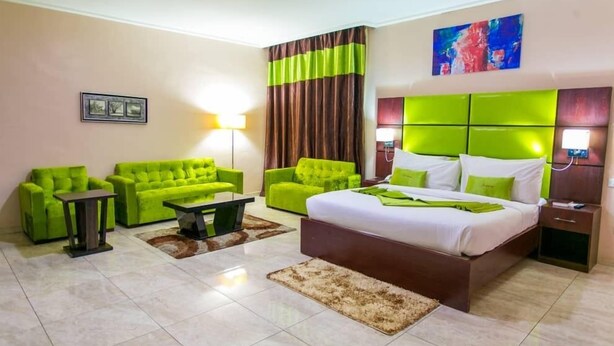A hotel room with a large bed, two green sofas, a small table, and a lamp. - De Santos Hotel (Lagos)