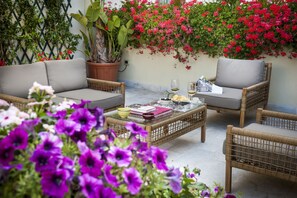 Un espace patio aménagé avec des meubles en osier, une table basse avec des livres et des verres, et une plante en pot.
