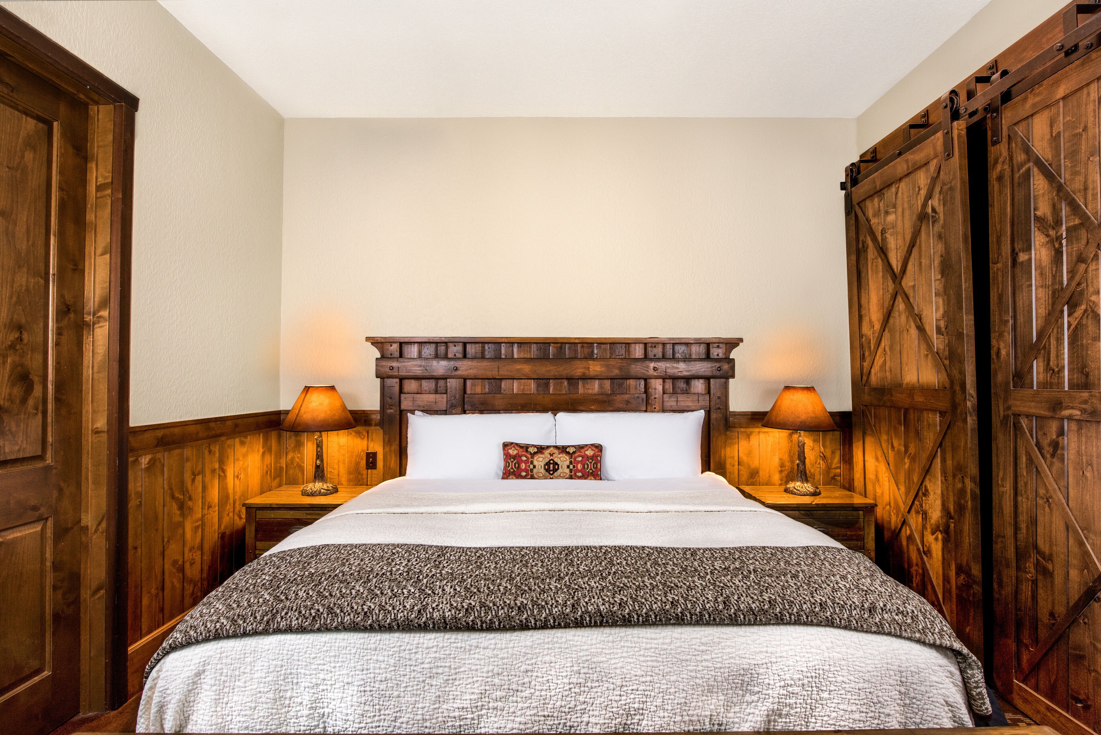 A bedroom with a wooden headboard, two bedside lamps, a patterned pillow, and a large bedspread.