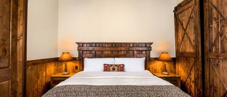 A bedroom with a wooden headboard, two bedside lamps, a patterned pillow, and a large bedspread.