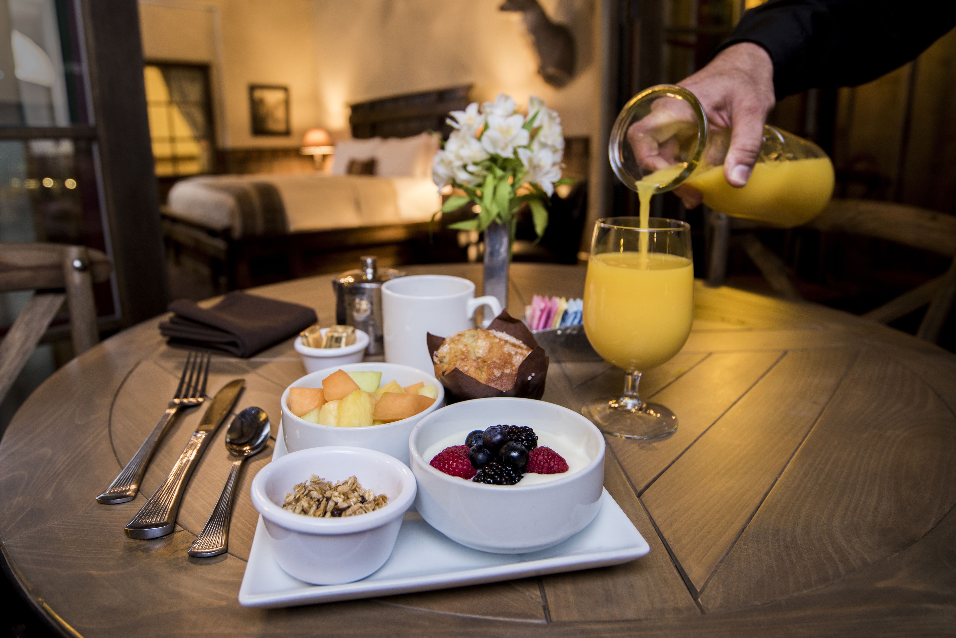 A breakfast table with a variety of food items, including fruits, yogurt, and a glass of orange juice.