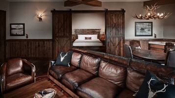A rustic interior with a leather sofa, wooden walls, a bed with a wooden headboard, and a chandelier.