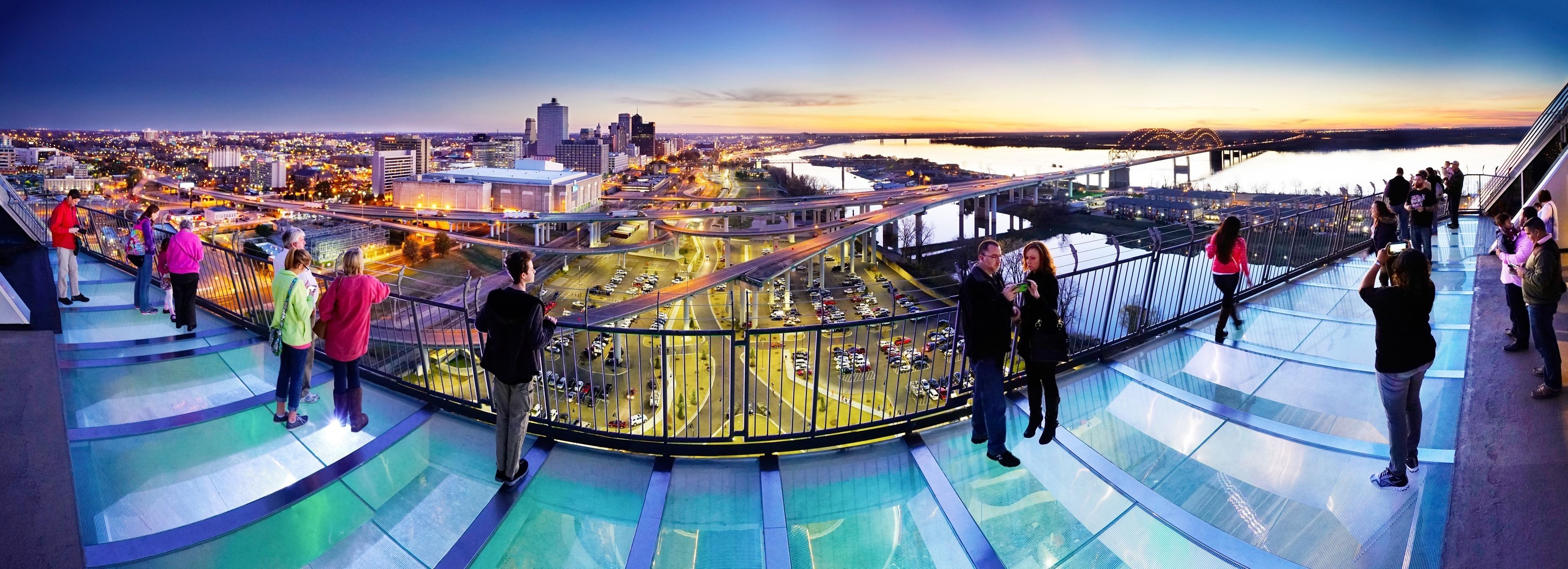 A panoramic view of a cityscape at dusk with a prominent bridge and a river.