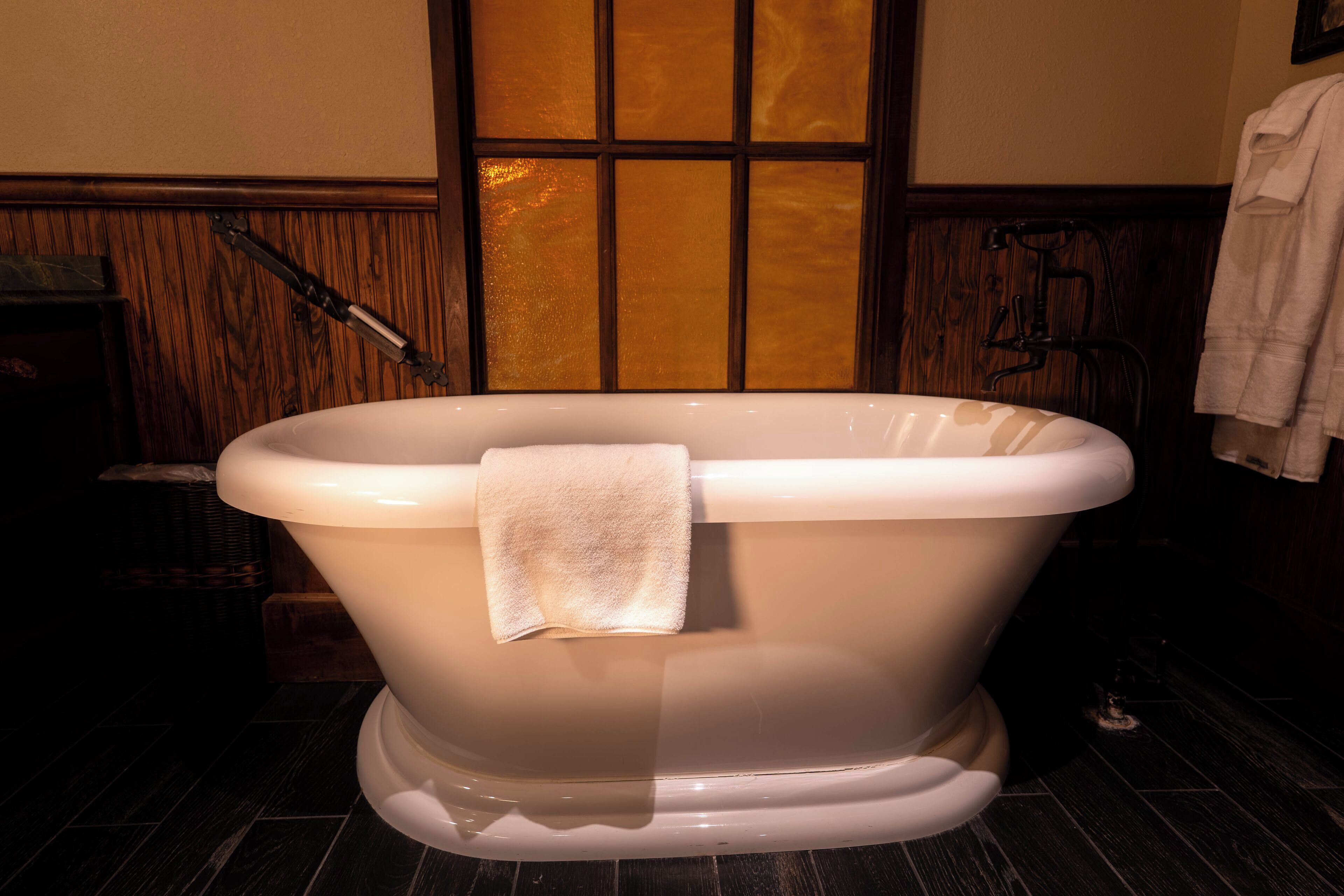 A freestanding bathtub with a towel, wooden paneling, and a window in the background.