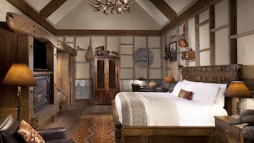 Quarto rústico com vigas de madeira aparentes, uma cama grande com cabeceira de madeira, um candelabro e um armário de madeira.