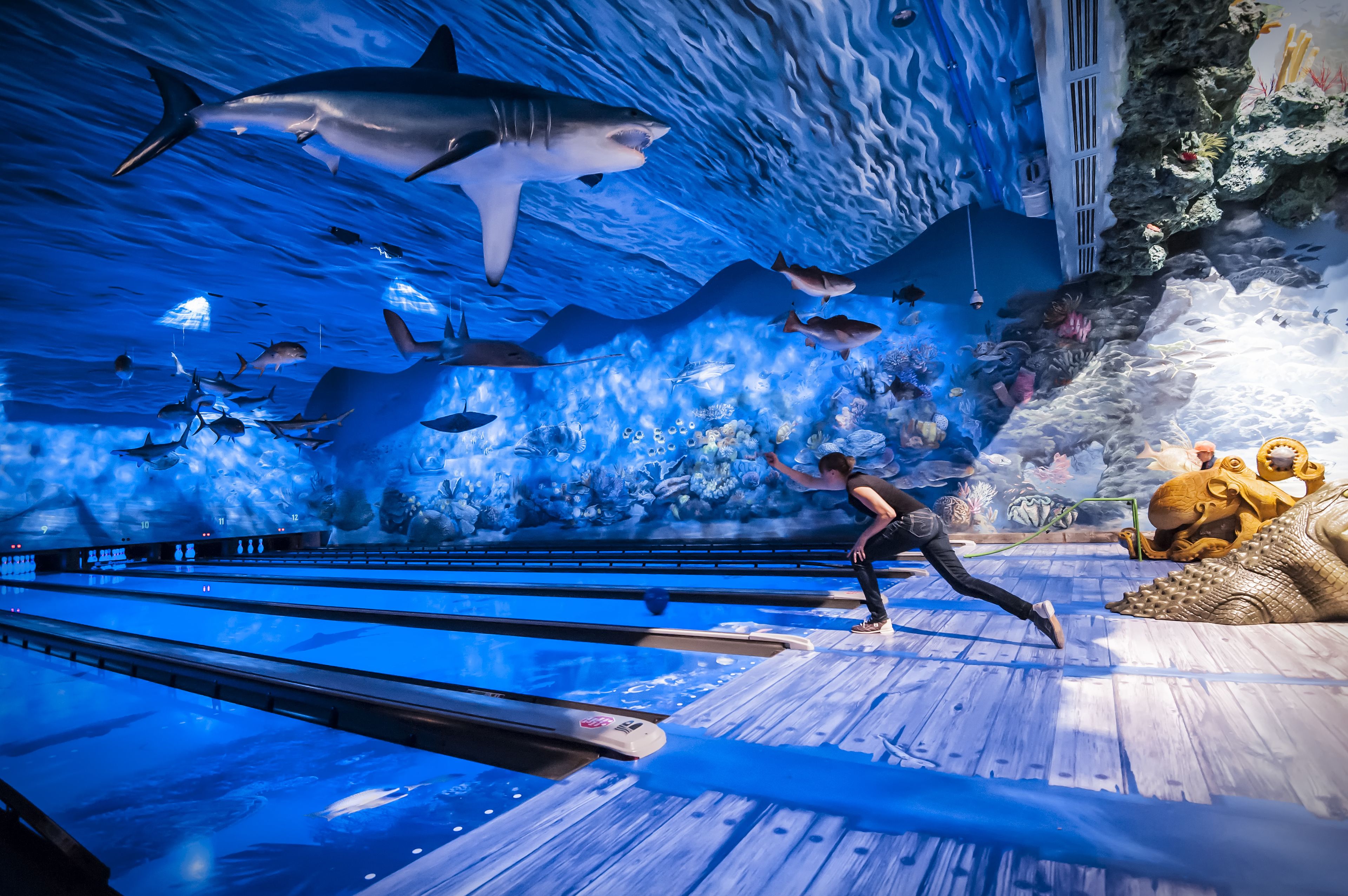 A bowling alley with a large aquarium wall displaying various marine life.