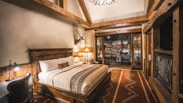 Une pièce chaleureuse avec un grand lit, des poutres apparentes, une tête de cerf accrochée au mur et une cheminée.