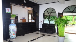 A reception area with a black reception desk, a large decorative vase, two black chairs, and a large potted plant. - Jayasinghe Holiday Resort (Kataragama)