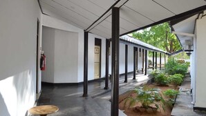 A covered corridor with a row of columns, a small table, and a garden area with plants. - Jayasinghe Holiday Resort (Kataragama)