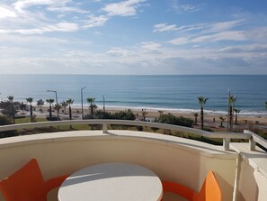 A balcony with a table and chairs, overlooking a beach with palm trees and a clear sky. - Belle Ocean Apart Hotel (Alanya)