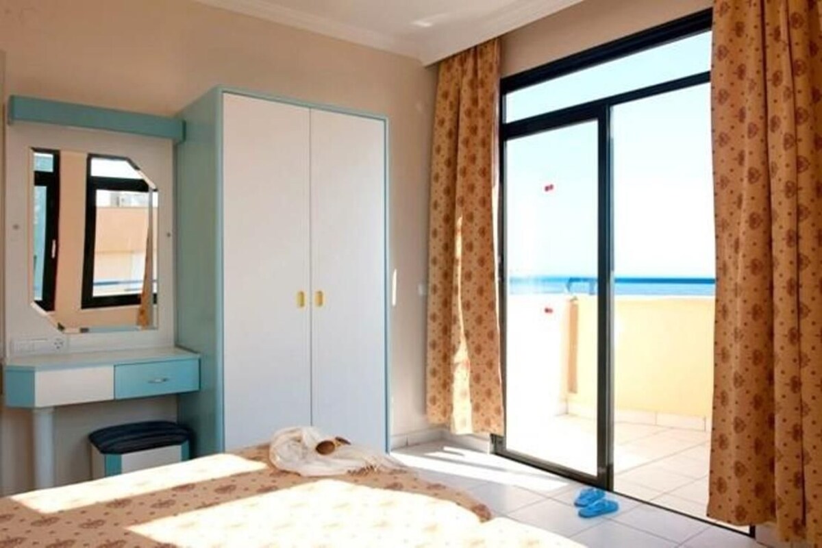 A bedroom with a bed, a wardrobe, a desk, and a large window with curtains.