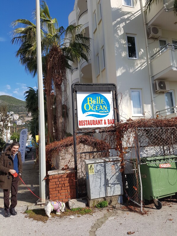 A sign for Belle Ocean, a restaurant and bar, with a view of a building and palm trees in the background. - Belle Ocean Apart Hotel (Alanya)