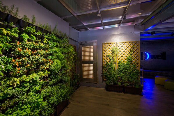 A modern indoor space with a vertical garden, wooden flooring, and a seating area with yellow cushions. - D'well Hostel (Kaohsiung)