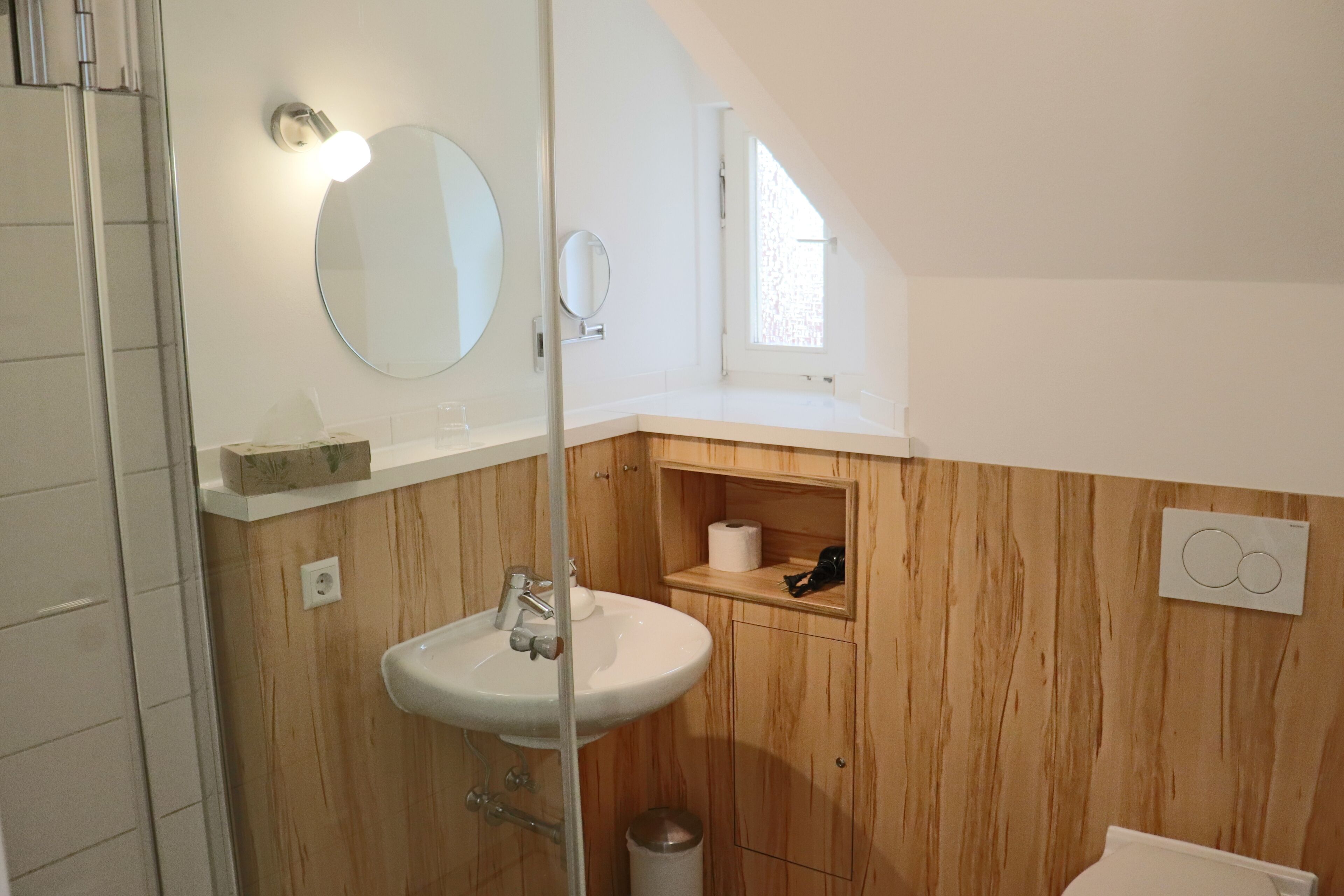 Un baño con tocador de madera, lavamanos, espejo y ventana que proporciona luz natural.