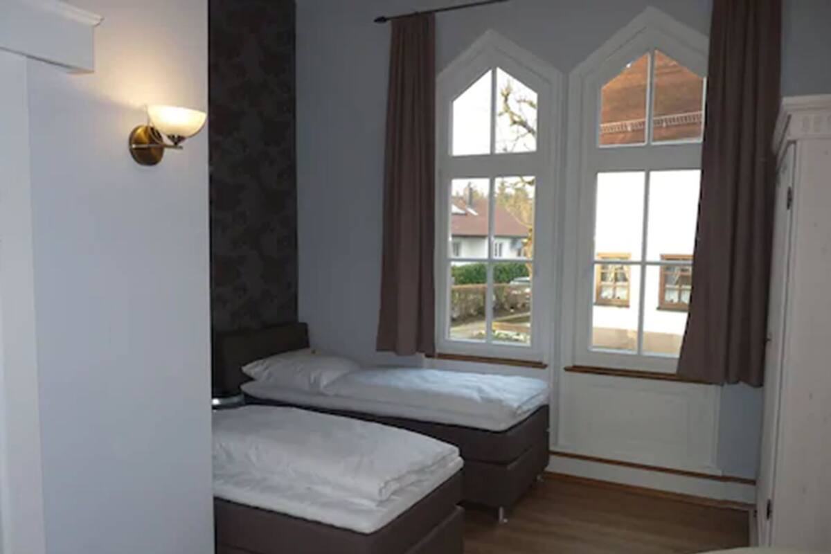 Een slaapkamer met twee bedden, een raam met gordijnen en een wandlamp.
