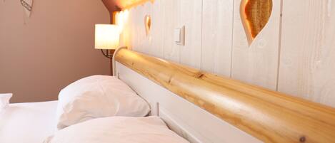 Un dormitorio con cabecera de madera, dos camas, una mesita de noche y una lámpara de pared.
