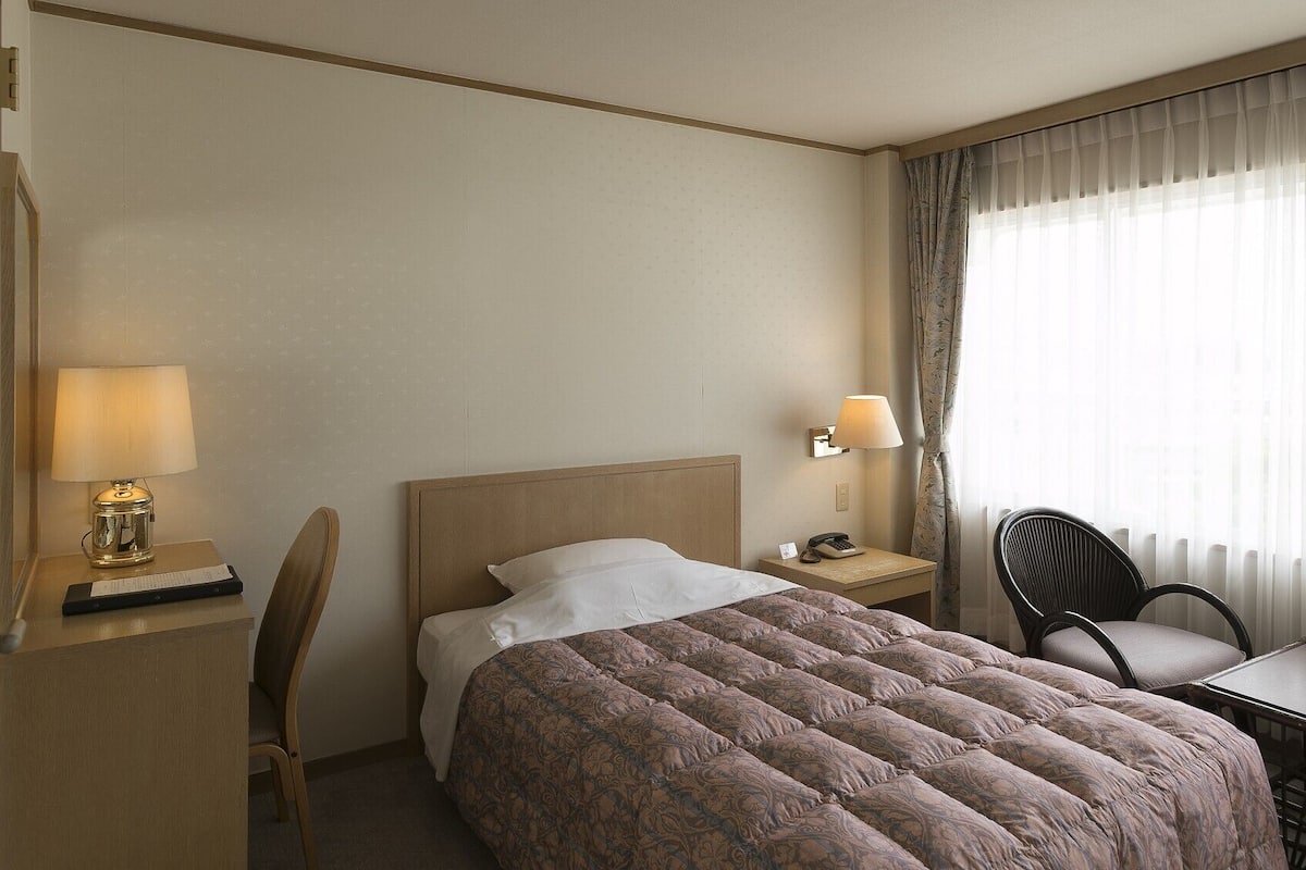 Una habitación de hotel con una cama, un escritorio con lámpara, una silla y una mesa.
