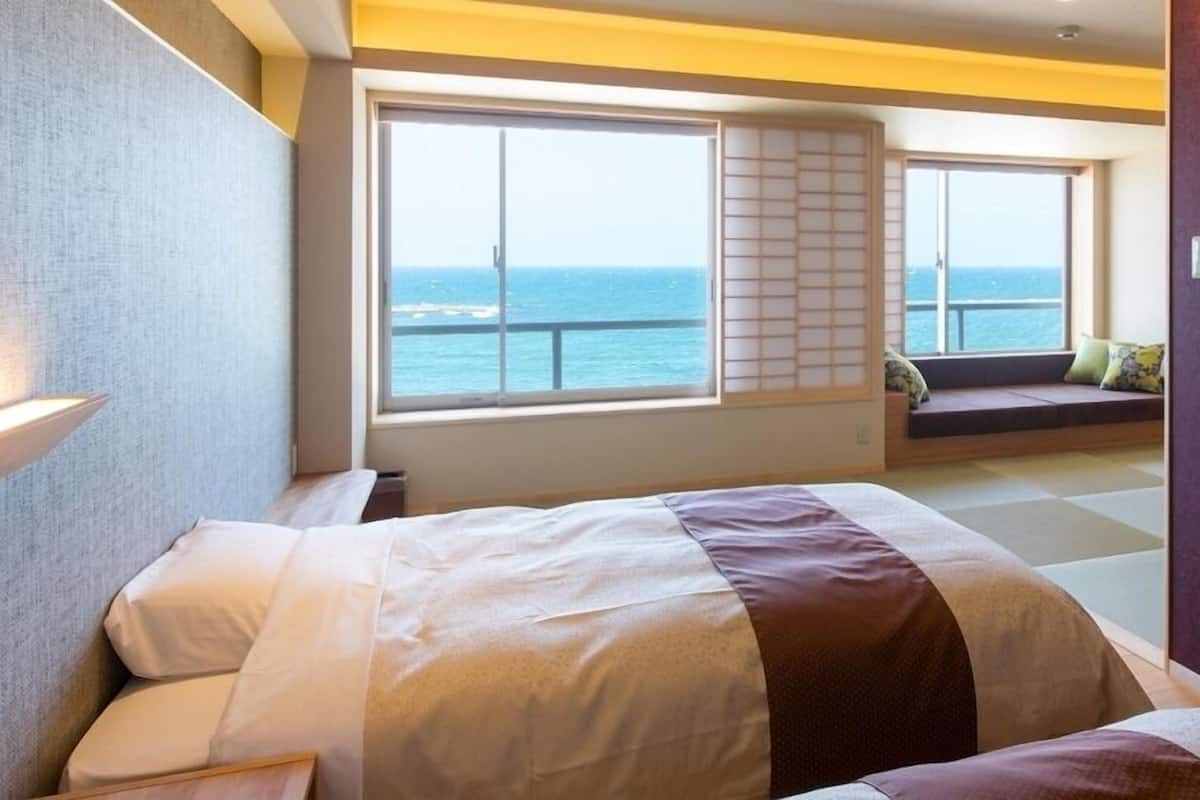 Habitación de hotel con cama, ventana vista al mar y zona de estar con cojines.