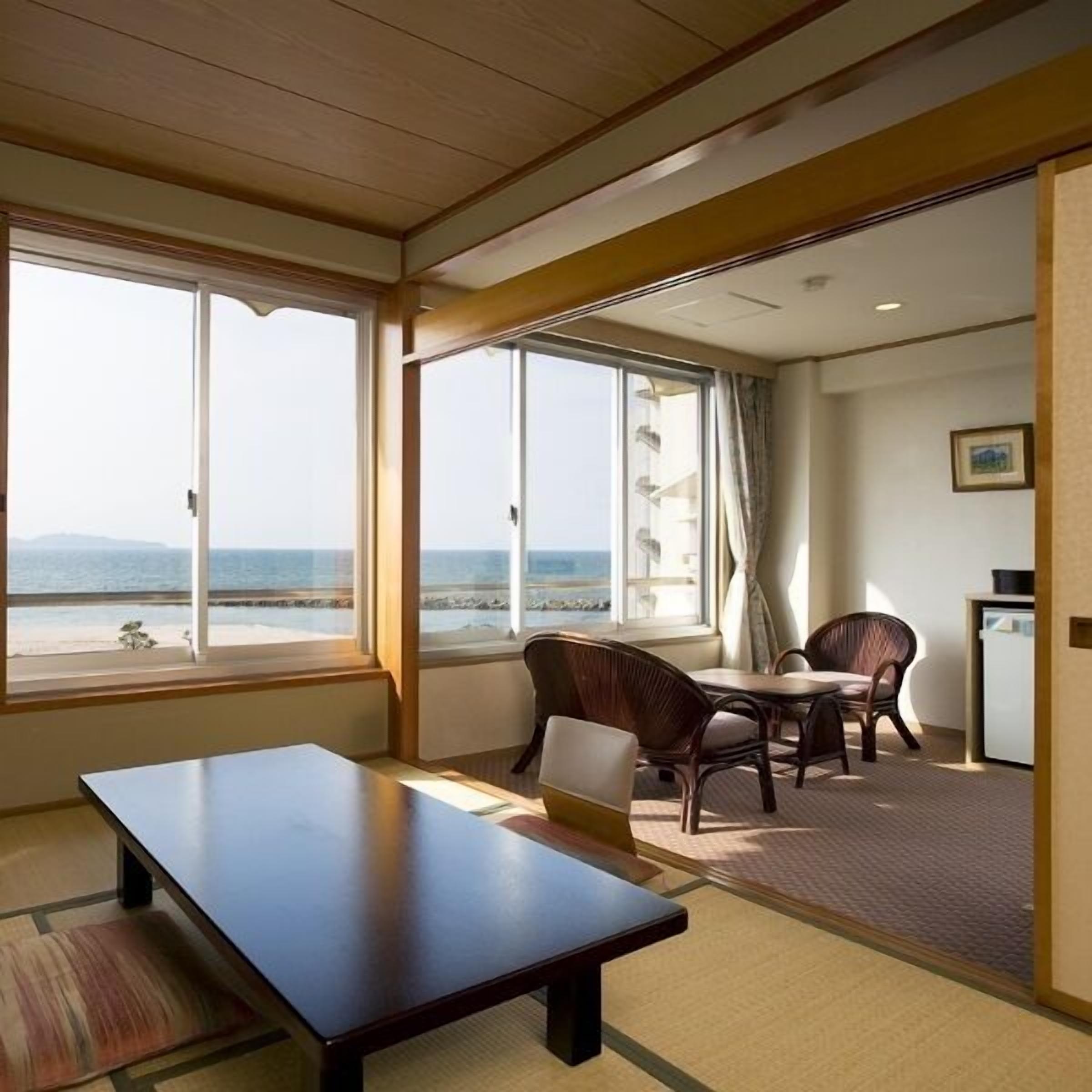 Quarto com uma grande janela com vista para a praia, uma mesa de jantar e duas cadeiras.