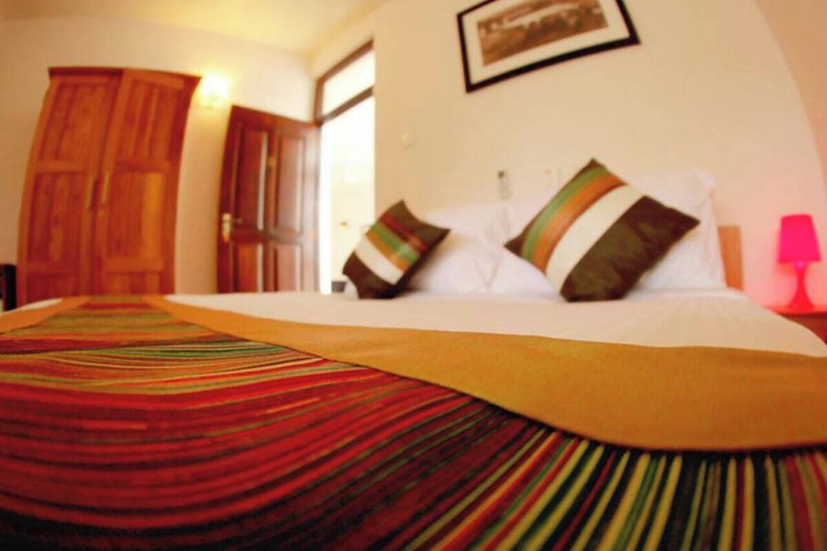 A bed with a striped bedspread, a wooden wardrobe, and a framed picture on the wall.