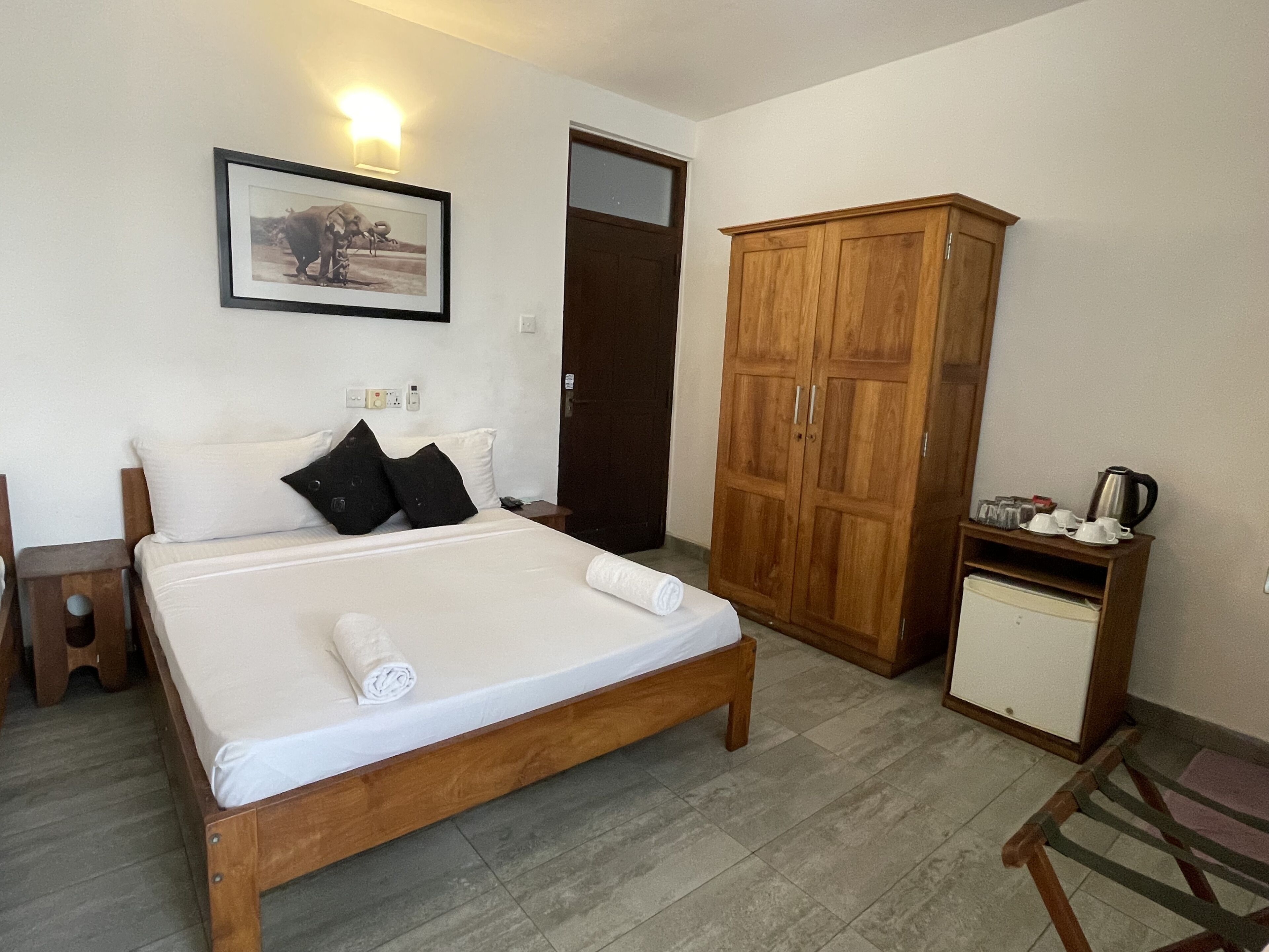 A bedroom with a wooden bed, a wardrobe, a small cabinet, and a framed picture on the wall.