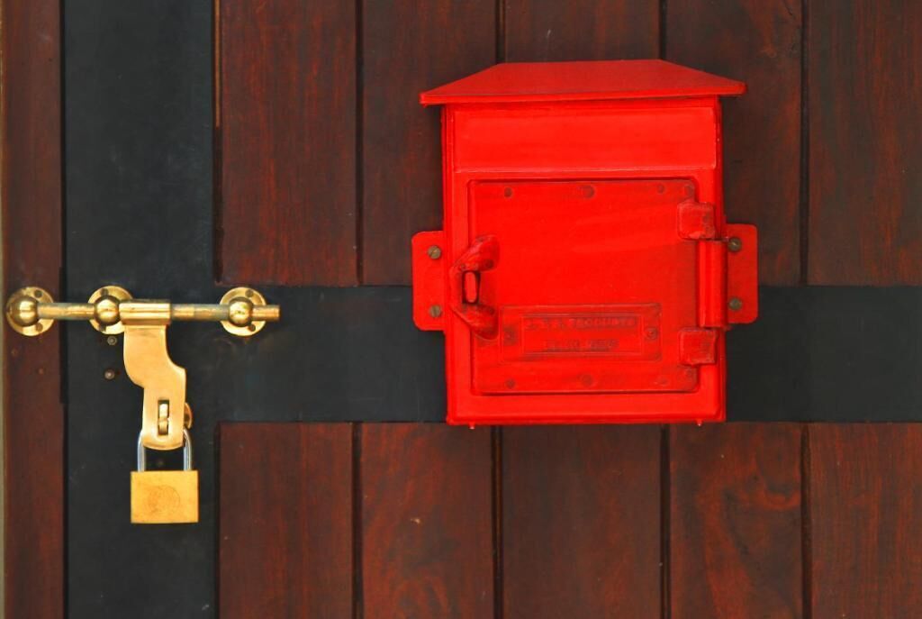 Una caja roja de alarma contra incendios fijada a una puerta de madera con cerradura y candado de bronce.
