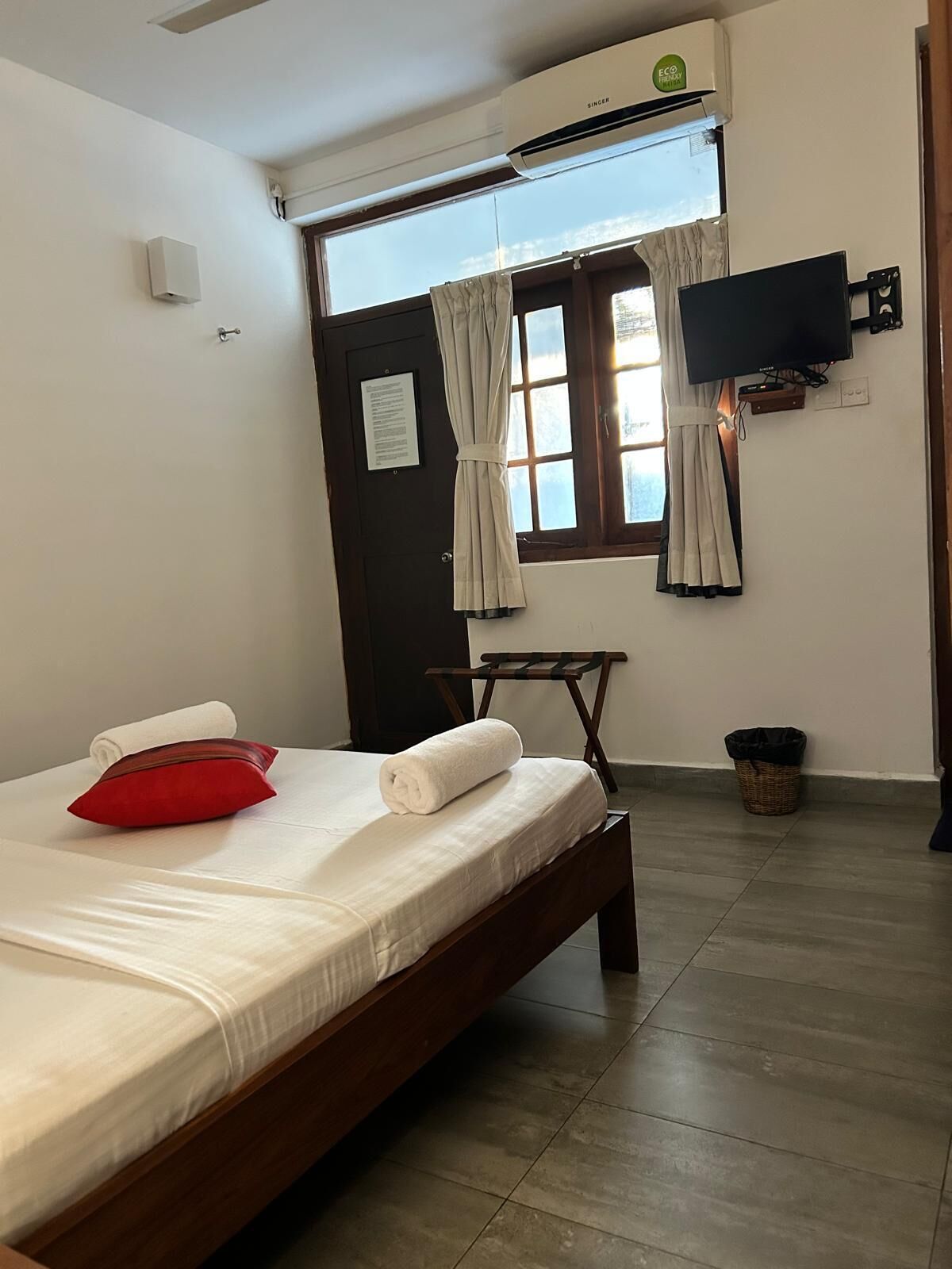 Hotelkamer met een bed, een aan de muur bevestigde televisie, een raam met gordijnen en een klein tafeltje.