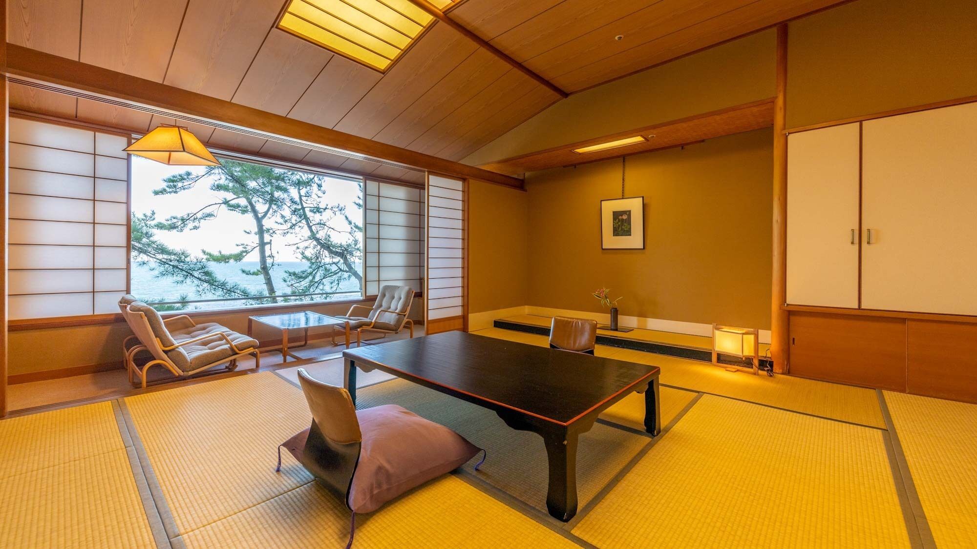 Et traditionelt japansk rum med tatamimåtter, et lavt bord, stole og havudsigt.