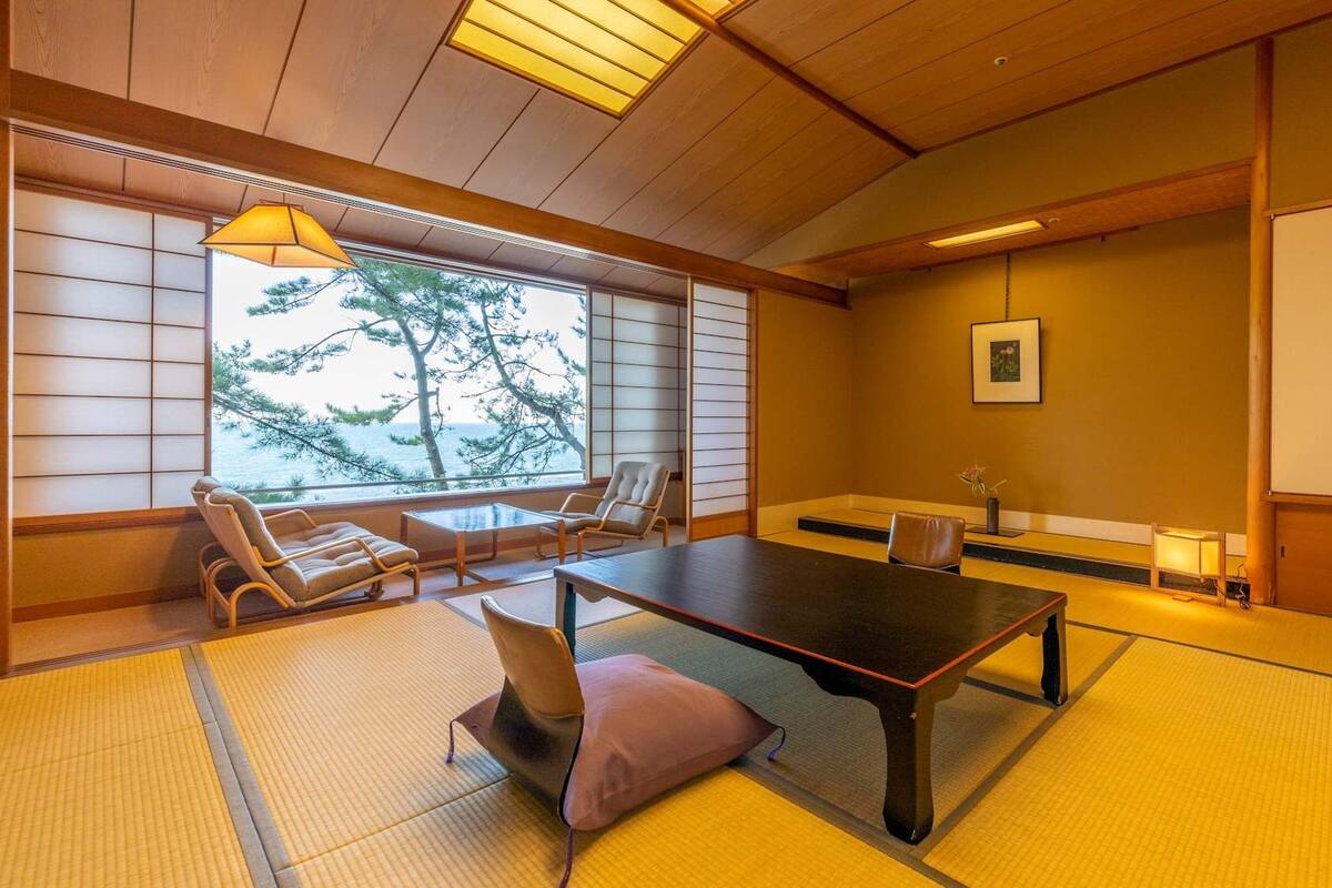 Una habitación japonesa tradicional con suelo de tatami, una mesa baja, sillas y vista al mar.