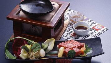 Una comida tradicional japonesa con una sartén negra, un tazón de salsa de soja y una variedad de verduras y carne en un plato negro.