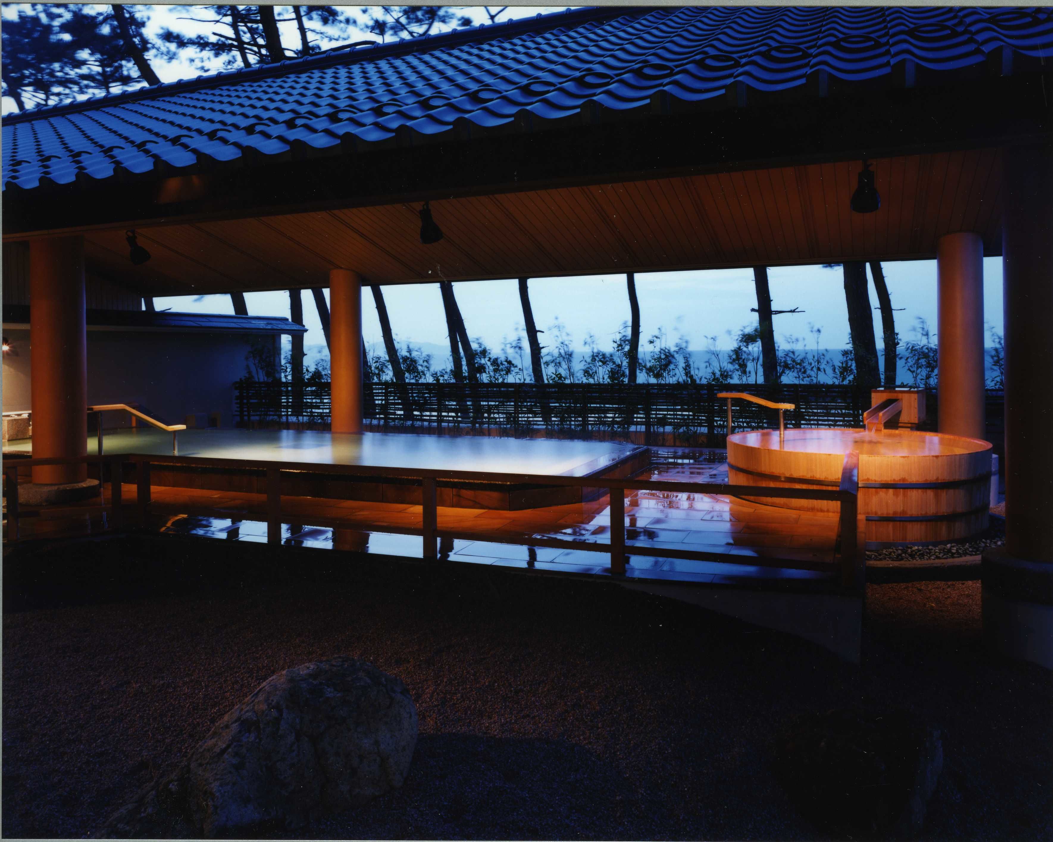 An outdoor hot spring area with a wooden deck, a stone basin, and a wooden table.