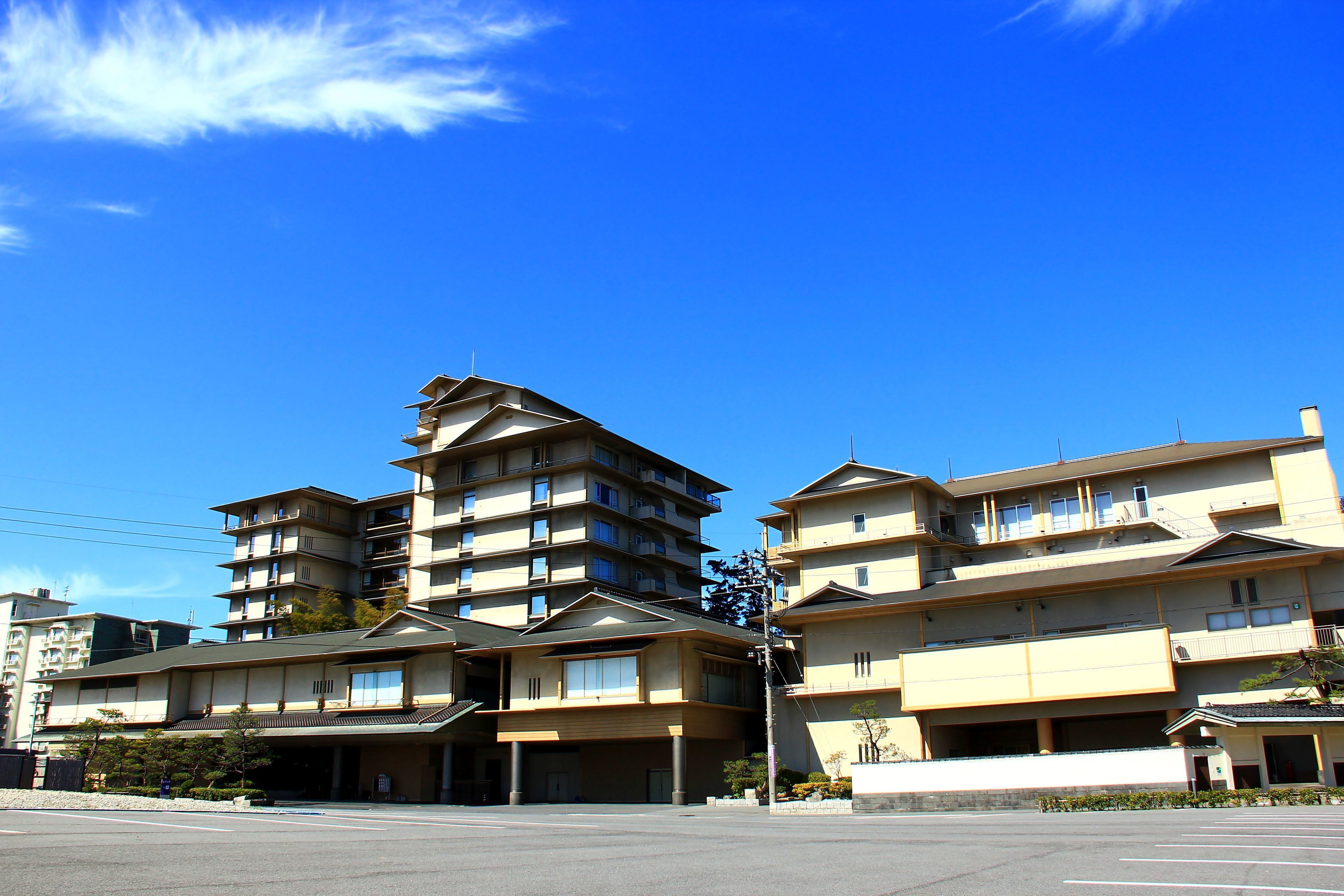 A multi-story hotel with a traditional architectural style, featuring multiple balconies and a parking lot in front.