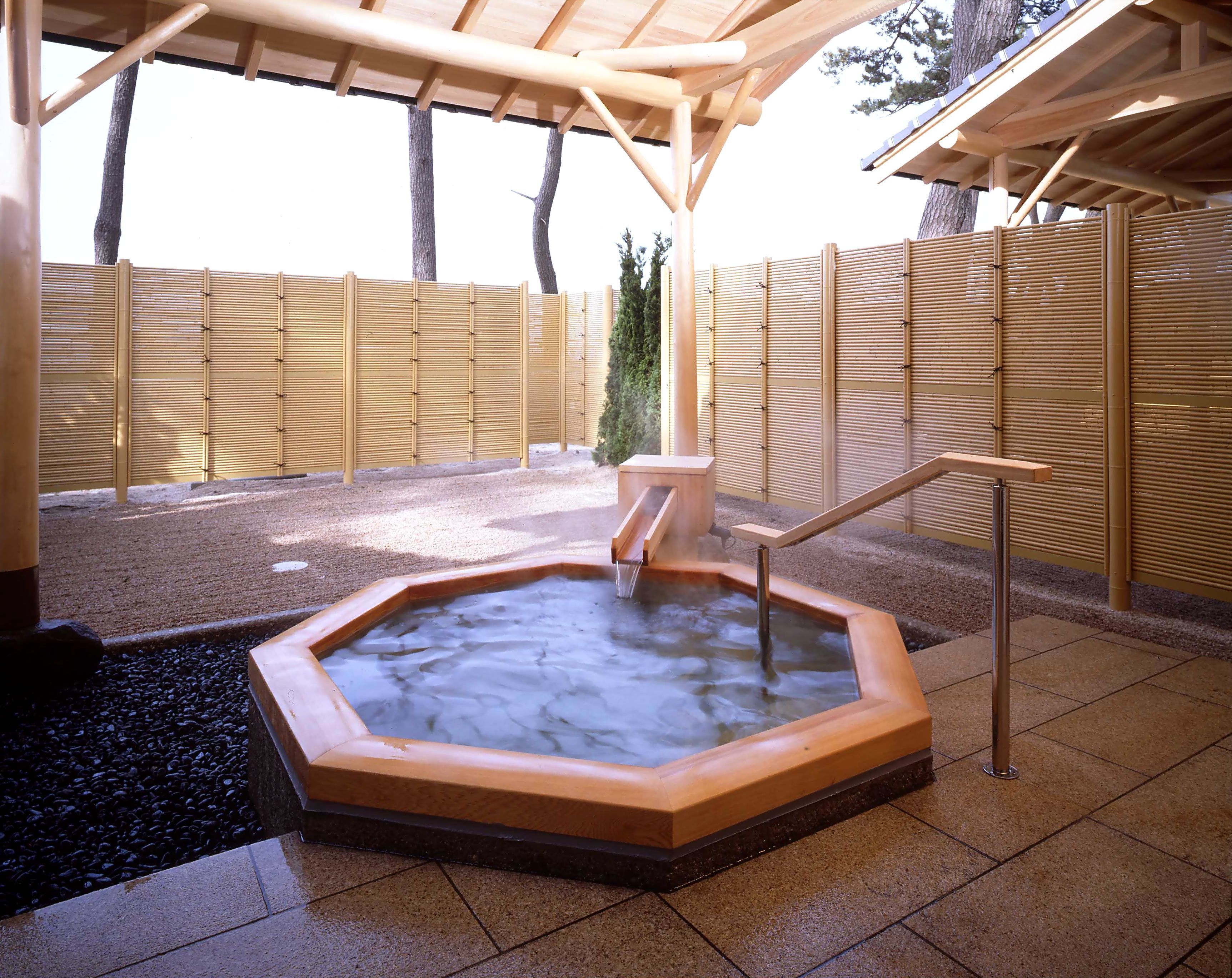 A hot spring area with a wooden deck, a hot tub, and a bamboo fence.