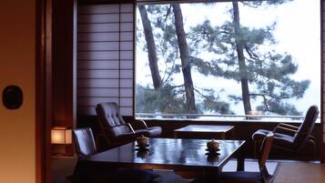 Ein traditioneller japanischer Raum mit Tatami-Bodenbelag, einem niedrigen Tisch mit Tee-Set und Blick auf Kiefern im Freien.