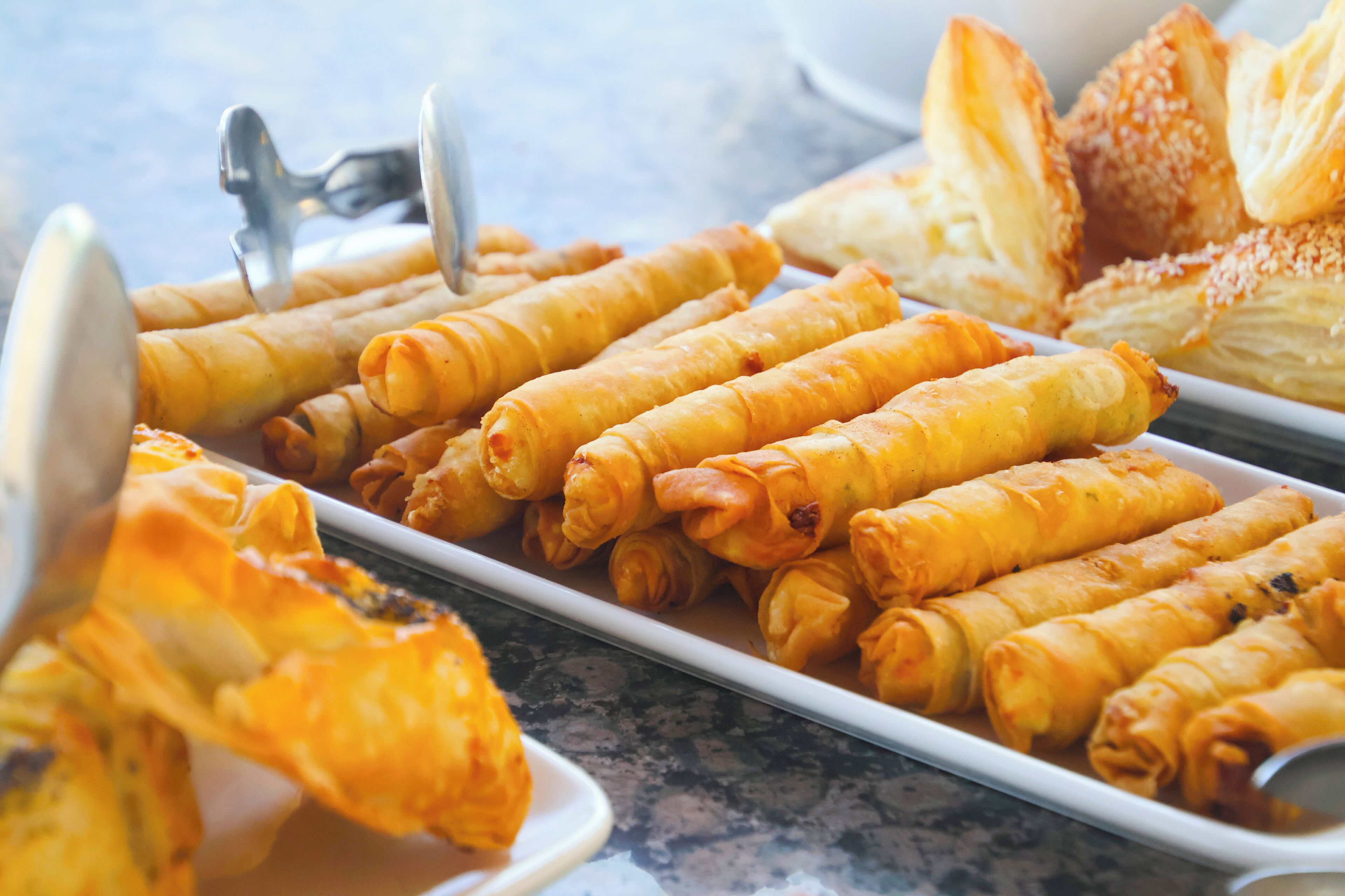 Buffet com rolinhos primavera, pão e uma colher.