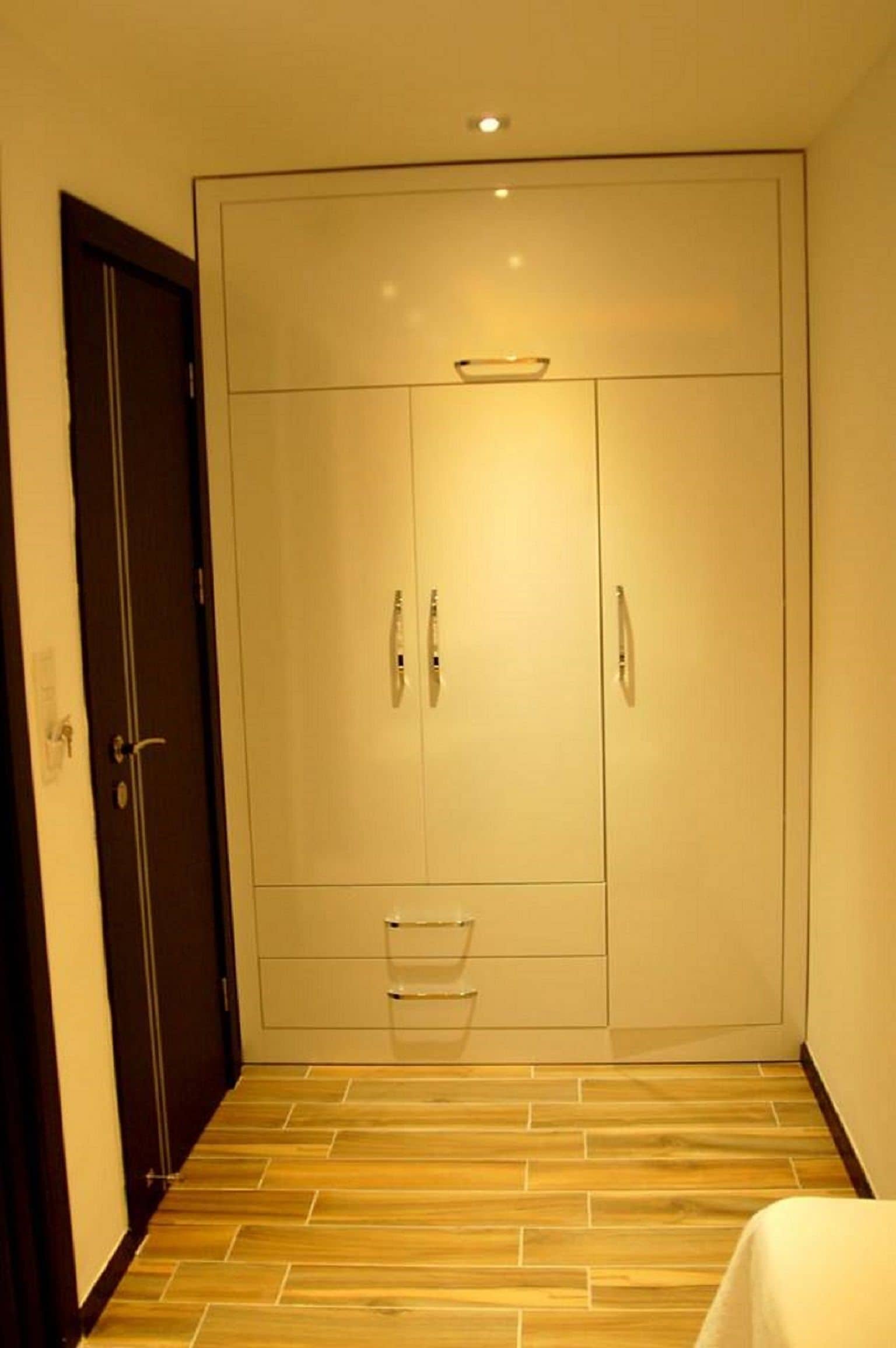 A room with a large wardrobe, a small shelf, and a wooden floor.