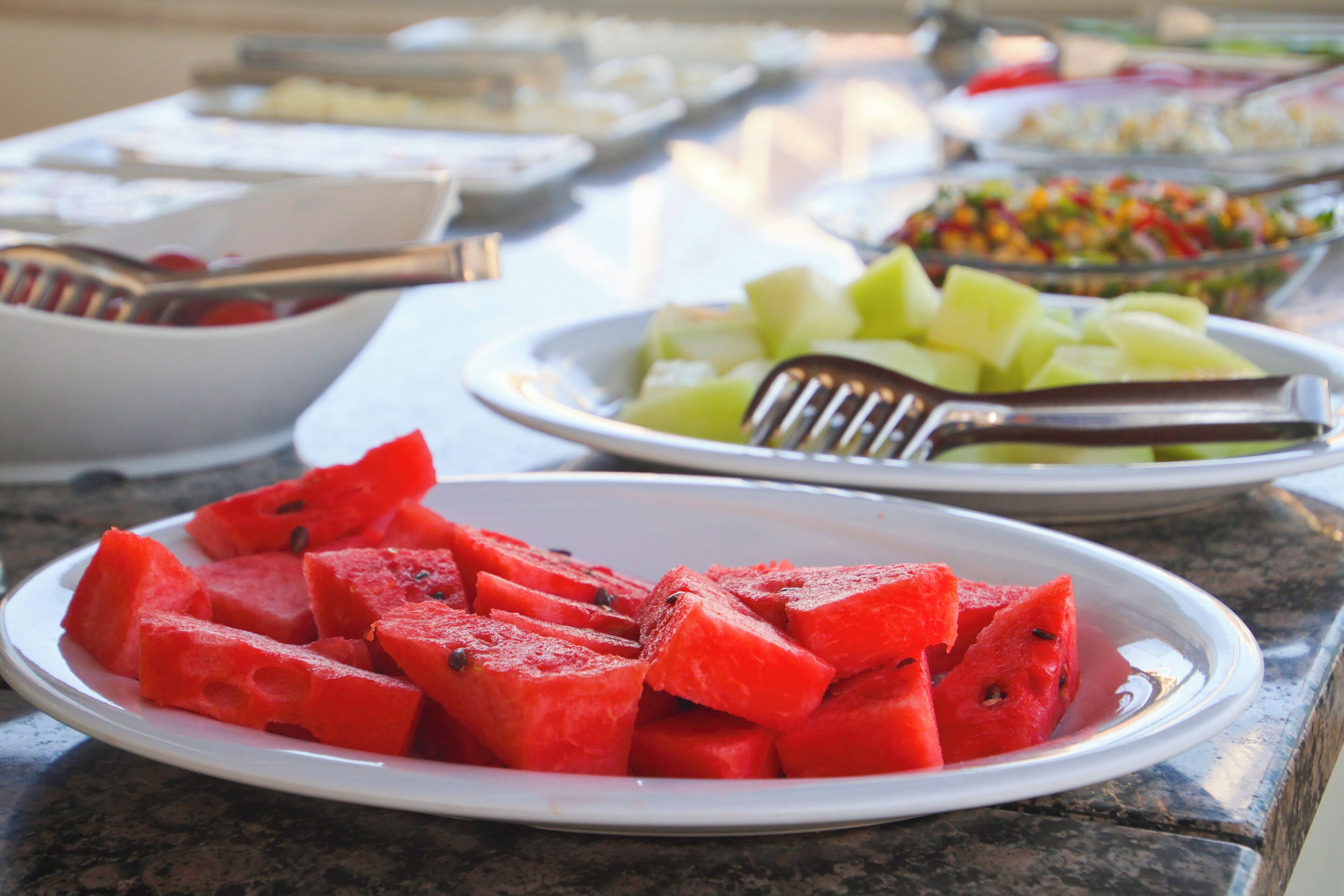 A table with various food items, including watermelon and a fruit salad.